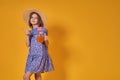 Little girl in a straw hat and sunglasses is smiling on a yellow background. child girl in a blue dress is holding a Royalty Free Stock Photo