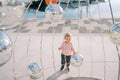 Little girl stretches her hands to a Christmas installation with mirror balls