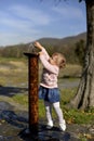 The little girl stretches her hands to the fountain.