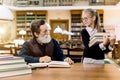 A little girl student pupil holding a lot of books in her hands and looking at her senior bearded teacher sitting at the Royalty Free Stock Photo