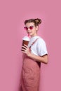 Little girl in sungalsses drinking fresh ice cocktail andlooking at camera on pink studio background Royalty Free Stock Photo