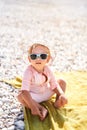 Little girl in sunglasses and panama sits on the beach