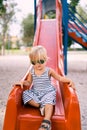 Little girl in sunglasses sits on a children slide