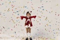 Little girl surprised by confetti wearing a Christmas themed dress with crown on her head, hands up smiling, isolated on Royalty Free Stock Photo