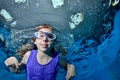 A little girl in swimming glasses is swimming underwater in the pool on a blue background and looking at me. Portrait. Close up. B Royalty Free Stock Photo