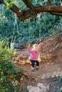 Little girl swings on a rope swing tied to a tree in the forest