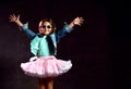 Little girl in blue t-shirt, denim jacket, poofy skirt, sneakers, sunglasses. Bouncing up against black background. Full length