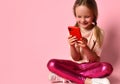 Little girl in a T-shirt, leggings and sneakers. Smiling woman using her red smartphone while sitting on floor with legs crossed Royalty Free Stock Photo