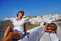 a little girl takes pictures of her mother against the beautiful views of Santorini
