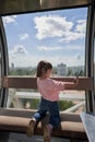 A little girl takes pictures of herself on her smartphone in the cab of a Ferris wheel against the background of a cloudy sky. Royalty Free Stock Photo