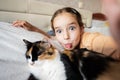 Little girl taking selfie with cat on bed at home. Portrait of adorable child show tongue with pet Royalty Free Stock Photo