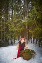 Little girl in thick coat and a red sash with basket of fir branches and red berries in cold winter day in forest