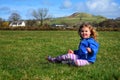 A little girl of toddler age sitting in a field with a big smile on her face. She is enjoying the moment. Hills in the background. Royalty Free Stock Photo