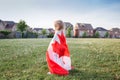 Little girl toddler wrapped in large Canadian flag walking in park meadow outdoor. Canada Day celebration outside. Kid covered Royalty Free Stock Photo