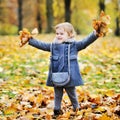 Little girl tossing leaves in autumn park