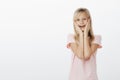 Little girl touched seeing cute pony. Indoor shot of pleased adorable female child with blond hair, holding hands on