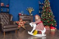 Little girl on a toy horse near a Christmas tree in blue home room Royalty Free Stock Photo