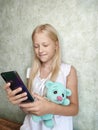 little girl with a toy teddy bear plays in a mobile phone Royalty Free Stock Photo