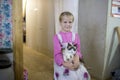 A little girl in a traditional dress stands with a kitten in her hands in the house