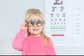 Little girl with trial frame near eye chart in hospital Royalty Free Stock Photo