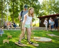 Little girl trying to walk on giant wooden feet in the park. Child playing funny outdoor game on sunny summer day. Family leisure