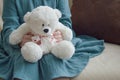 A little girl in a turquoise dress holds a white toy bear with a ribbon with hearts in her hands. a child`s toy. Royalty Free Stock Photo