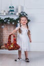 Little girl with two pigtails standing near a Christmas tree. She is holding a basket with toys Royalty Free Stock Photo