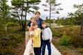 Little girl, two school boys and father walking on wooden path on black moor nature landscape. Active family with three