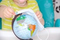 A little girl of two years old is sitting in a baby chair and is holding a medical mask in her hands. Child with a globe, globe Royalty Free Stock Photo