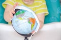 A little girl of two years old is sitting in a baby chair and is holding a medical mask in her hands. Child with a globe, globe Royalty Free Stock Photo