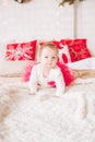 A little girl under one year old in an airy dress on a large bed in a room decorated for Christmas Royalty Free Stock Photo