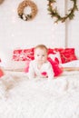 A little girl under one year old in an airy dress on a large bed in a room decorated for Christmas Royalty Free Stock Photo