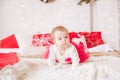 A little girl under one year old in an airy dress on a large bed in a room decorated for Christmas Royalty Free Stock Photo