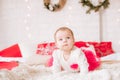 A little girl under one year old in an airy dress on a large bed in a room decorated for Christmas Royalty Free Stock Photo