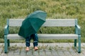 A little girl under an umbrella sits on a bench Royalty Free Stock Photo