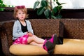 Little girl using laptop. Child in pink skirt and boots, sunglasses, grey top sitting at the sofa, playing . Looking the camera