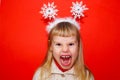 The little girl is very emotionally angry and expresses dissatisfaction. Red background. Portrait. Christmas decoration on the Royalty Free Stock Photo