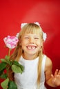 Little girl is very happy with the gift of flower. Pink rose in the hands of a girl. Birthday, holiday. Red background Royalty Free Stock Photo