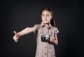 Little girl with vintage camera thumb up at black background Royalty Free Stock Photo