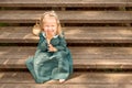 Little girl in vintage retro linen dress barefoot sitting and laughing on a wooden stairs in the park with Wicker basket Royalty Free Stock Photo