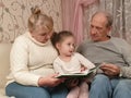 little girl visiting grandparents sitting with them on the couch and reading a book Royalty Free Stock Photo