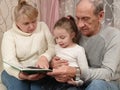 little girl visiting grandparents sitting with them on the couch and reading a book Royalty Free Stock Photo