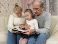 little girl visiting grandparents sitting with them on the couch and reading a book Royalty Free Stock Photo