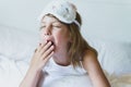 Little girl wakes up in morning yawning with closed eyes, sitting on bed wearing white cat, bunny sleep mask. Early morning wake Royalty Free Stock Photo