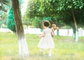 A little girl walking in green park in a white dress with a doll