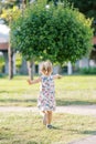 Little girl walks across a sunny lawn towards a green tree waving her arms. Back view Royalty Free Stock Photo