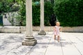 Little girl walks along a tiled path near the columns against the background of green magnolia bushes