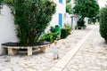 Little girl walks through the cobbled courtyard near the house, a bench and greenery. Back view Royalty Free Stock Photo