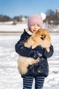 Little girl in warm clothes holding on hnds and hugging dog pet Pomeranian Spitz