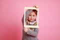 Portrait of child looking through frame on rosa bachground